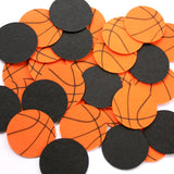 A pile of round cardstock 1 inch circles designed like orange basketballs with black lines along with black solid circles on a white background.