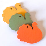 Turkey shaped cardstock paper tags in orange, olive green, and golden yellow, arranged diagonally on a white background.
